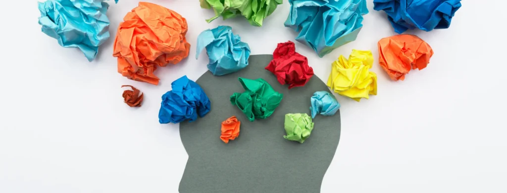 Silhueta de cabeça humana com papel amassado colorido ao redor simbolizando pensamentos e emoções diversificados.