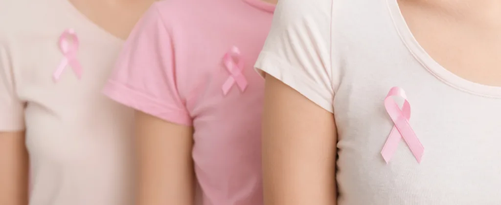 Três mulheres vestindo camisetas com laços rosa simbolizando a conscientização do Outubro Rosa para a prevenção do câncer de mama.