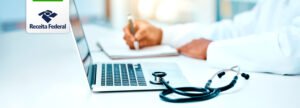 Médico preenchendo informações em um caderno com um laptop e estetoscópio sobre a mesa, representando a nova plataforma Receita Saúde da Receita Federal.