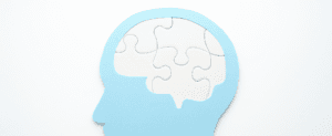 Silhueta de cabeça azul com um cérebro formado por peças de quebra-cabeça brancas, simbolizando a complexidade da saúde mental.