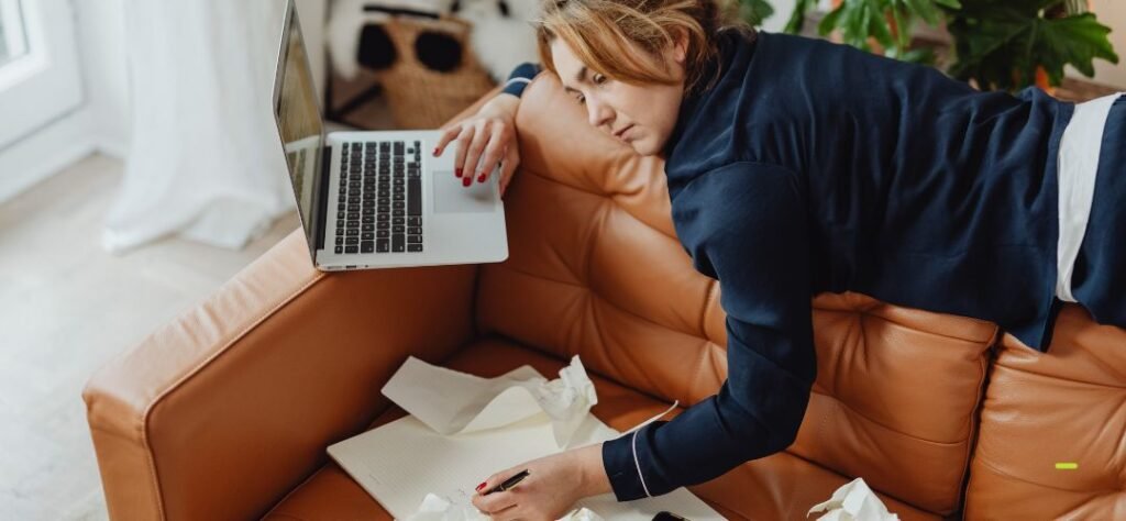 Profissional de saúde exausta trabalhando com notebook e anotações em ambiente doméstico.