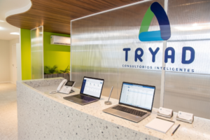 Recepção da TRYAD Consultórios Inteligentes, com balcão de atendimento, notebooks e identidade visual da marca em destaque.